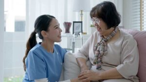 An older adult uses a tablet at a table while a caregiver points to the screen.